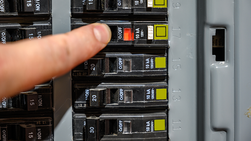 Person identifying tripped circuit breaker in fuse box—troubleshooting why breaker keeps tripping during heat